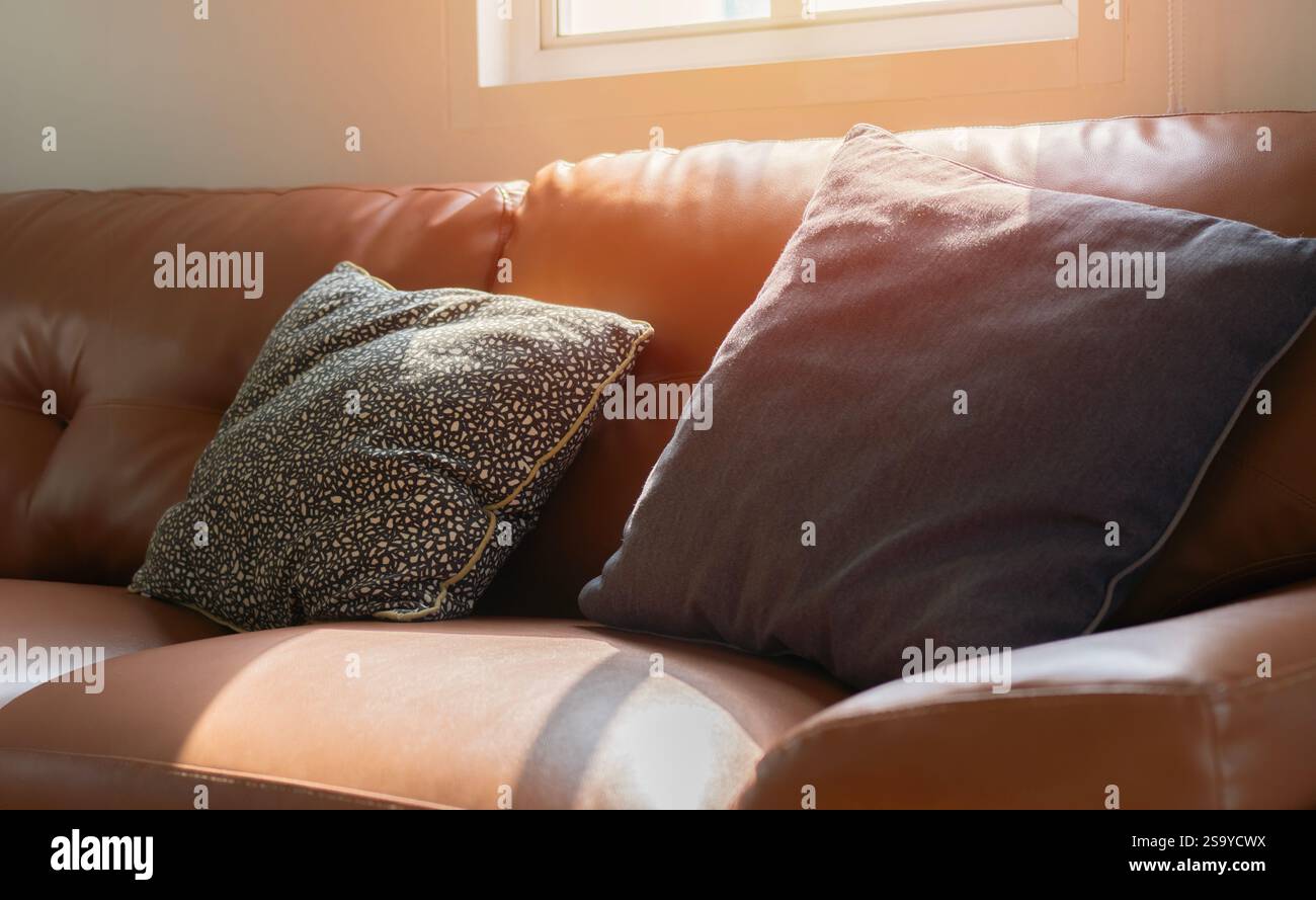 Comodi divani e cuscini in pelle arancione con una luce soffusa del sole proveniente dalla finestra posteriore. Concetto di stile di vita. Foto Stock