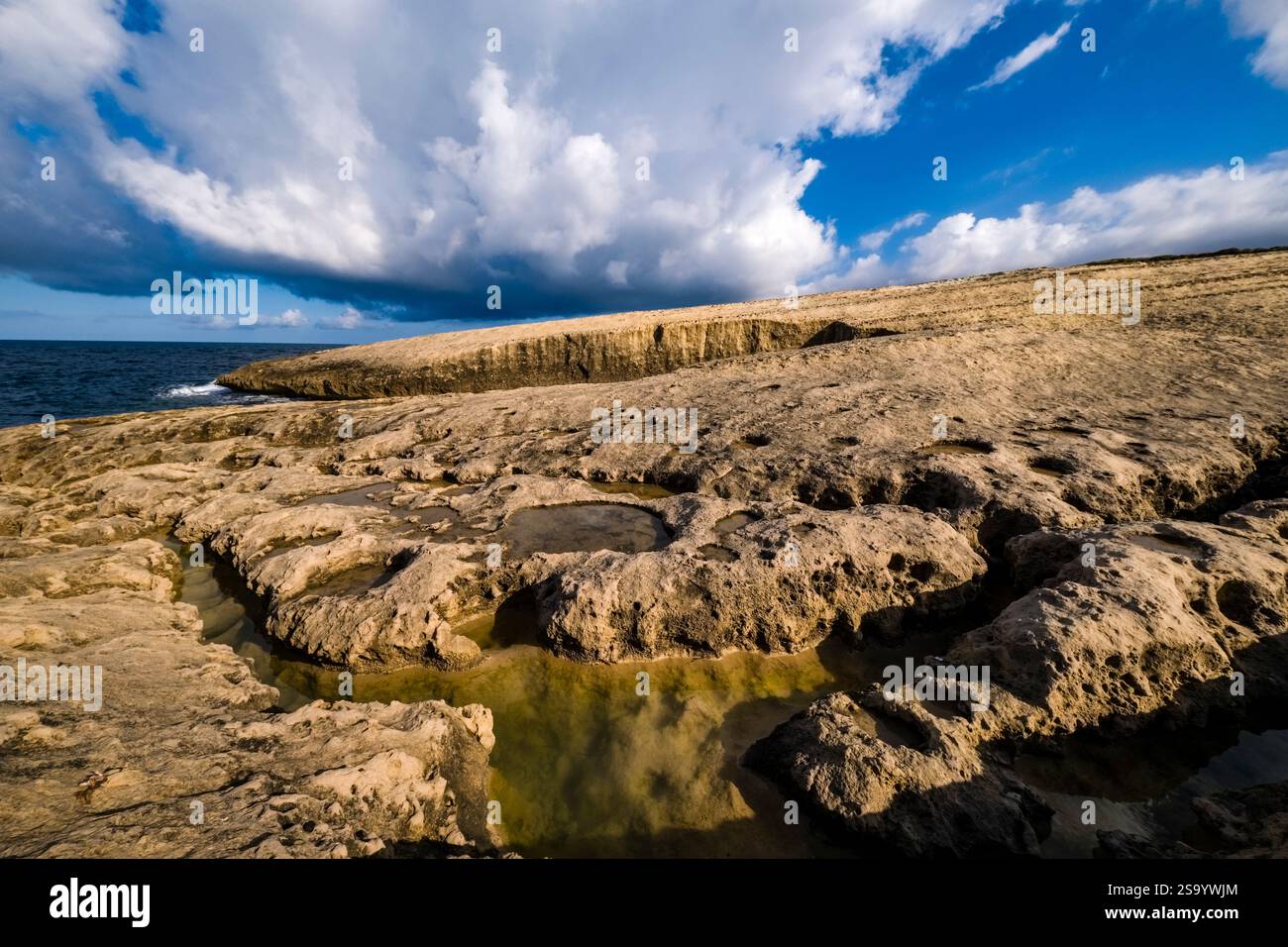 Acqua piovana in piccoli fori d'acqua sulla costa rocciosa intorno alla grotta Scoglio del Genovese, cielo blu con nuvole bianche in lontananza. Foto Stock