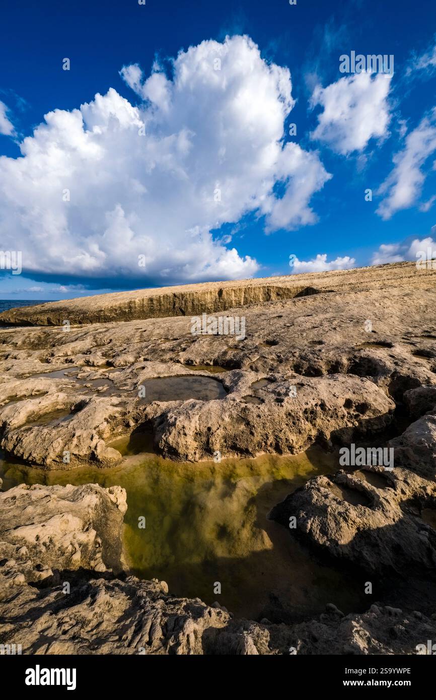 Acqua piovana in piccoli fori d'acqua sulla costa rocciosa intorno alla grotta Scoglio del Genovese, cielo blu con nuvole bianche in lontananza. Foto Stock