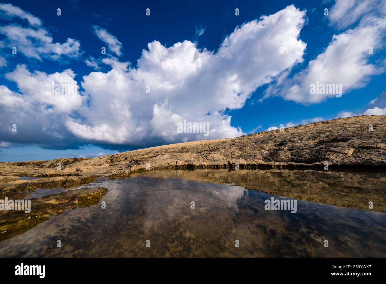 Acqua piovana in piccoli fori d'acqua sulla costa rocciosa intorno alla grotta Scoglio del Genovese, cielo blu con nuvole bianche in lontananza. Foto Stock