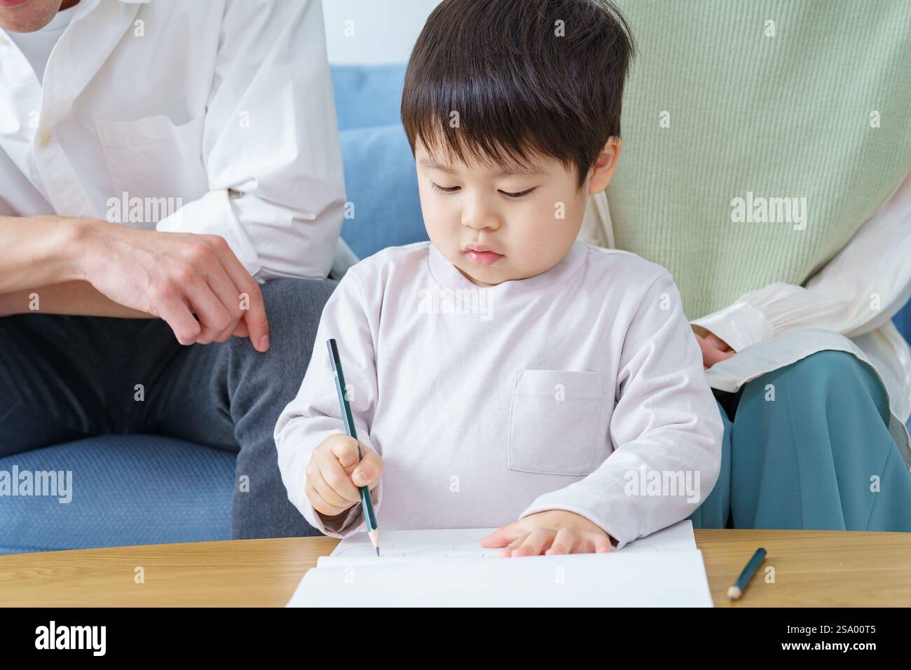 Ragazzo che disegna con matita e genitori che guardano Foto Stock