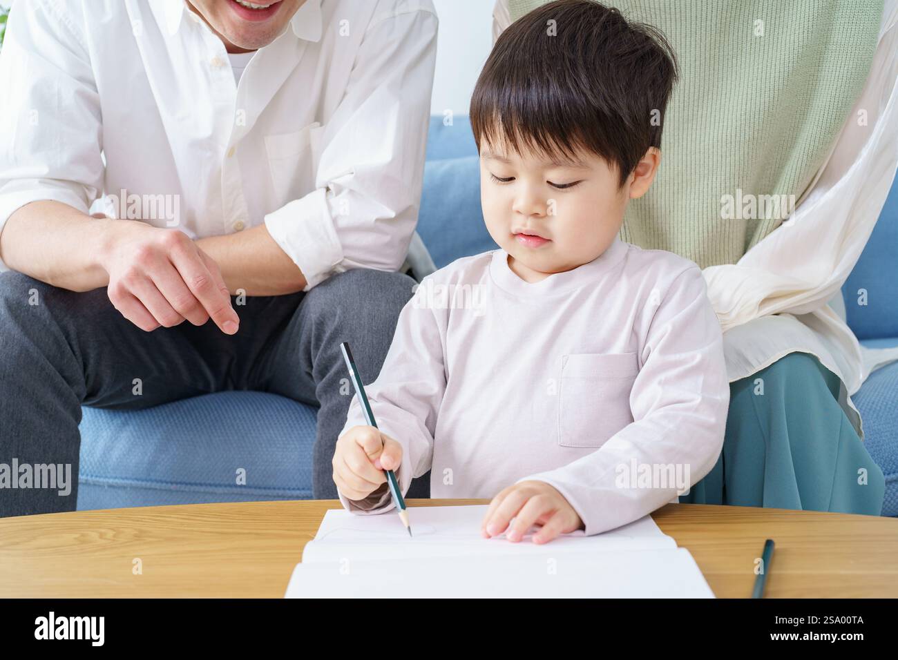 Ragazzo che disegna con matita e genitori che guardano Foto Stock