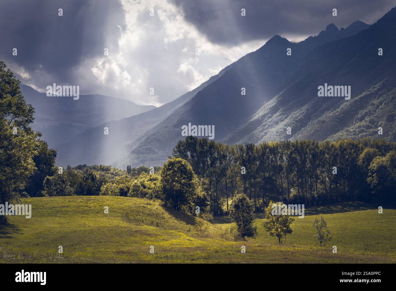 I raggi del sole penetrano attraverso nuvole scure, illuminando il vibrante paesaggio del Parco naturale Posets-Maladeta nei Pirenei spagnoli Foto Stock