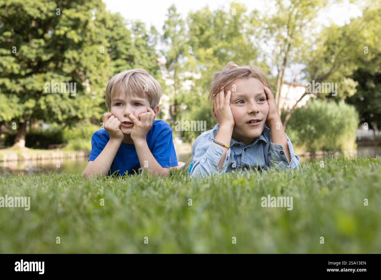 ritratto di due ragazzi di 8 anni sdraiati sull'erba e che mostrano noia. Un momento di riposo e riflessione. fratelli in una passeggiata nel parco. Vacanze estive Foto Stock