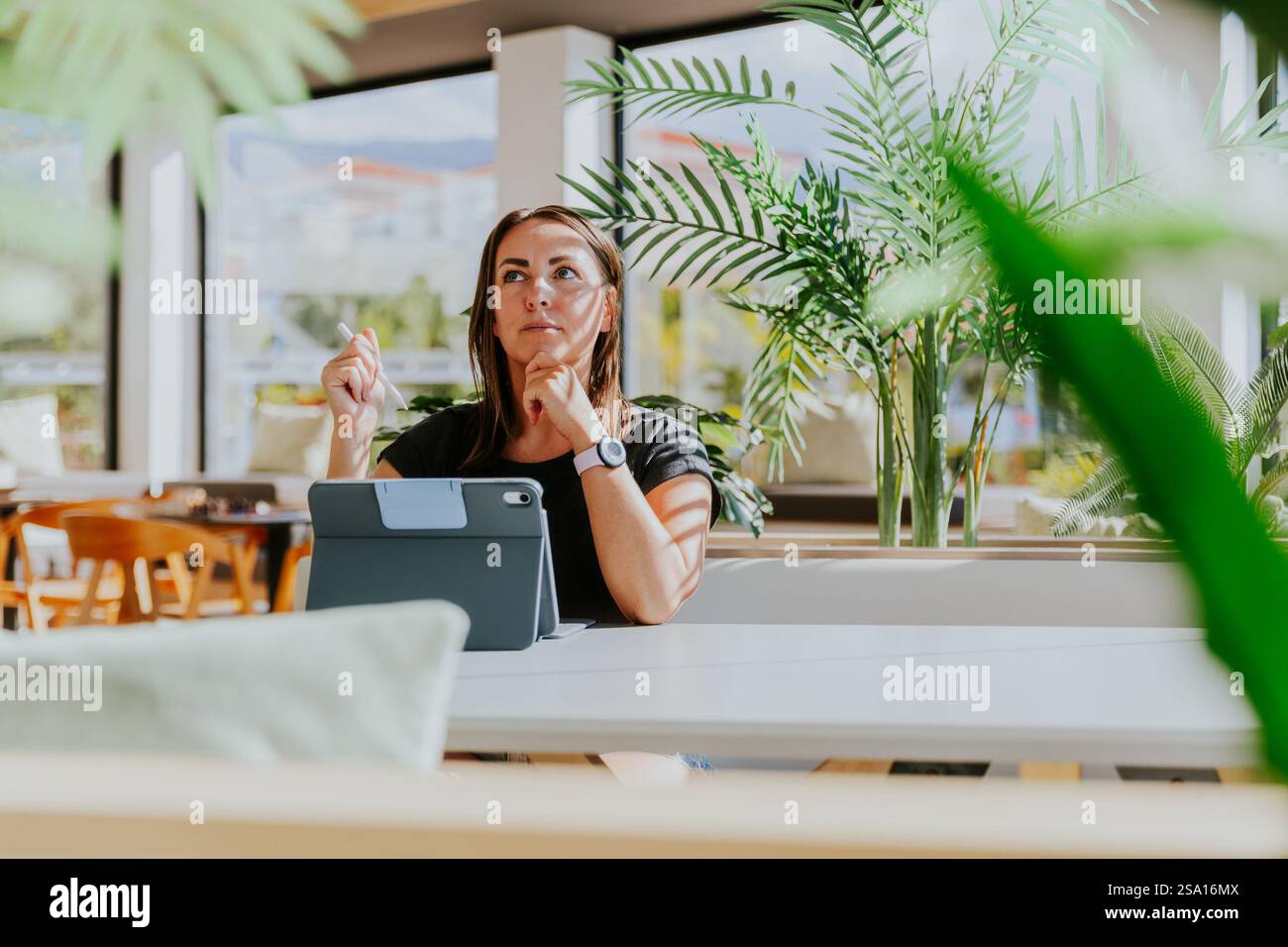 Una donna è seduta a un tavolo con un tablet di fronte a lei e ha un'espressione premurosa. Foto Stock