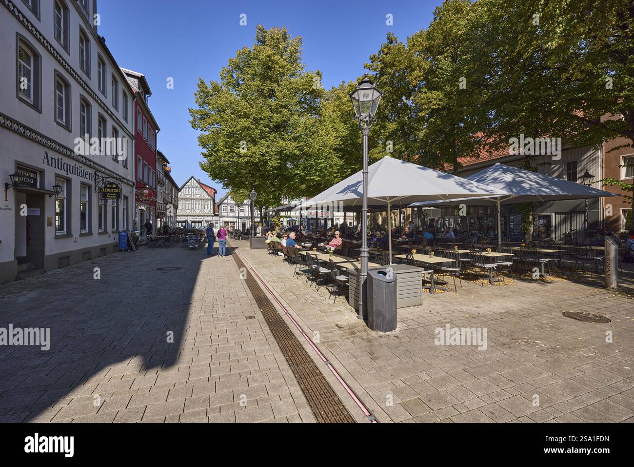 Zona pedonale, piazza, area esterna di un ristorante con tavoli, sedie e ombrellone, lanterna, alberi, architettura generale, cielo blu senza nuvole, Brand Foto Stock