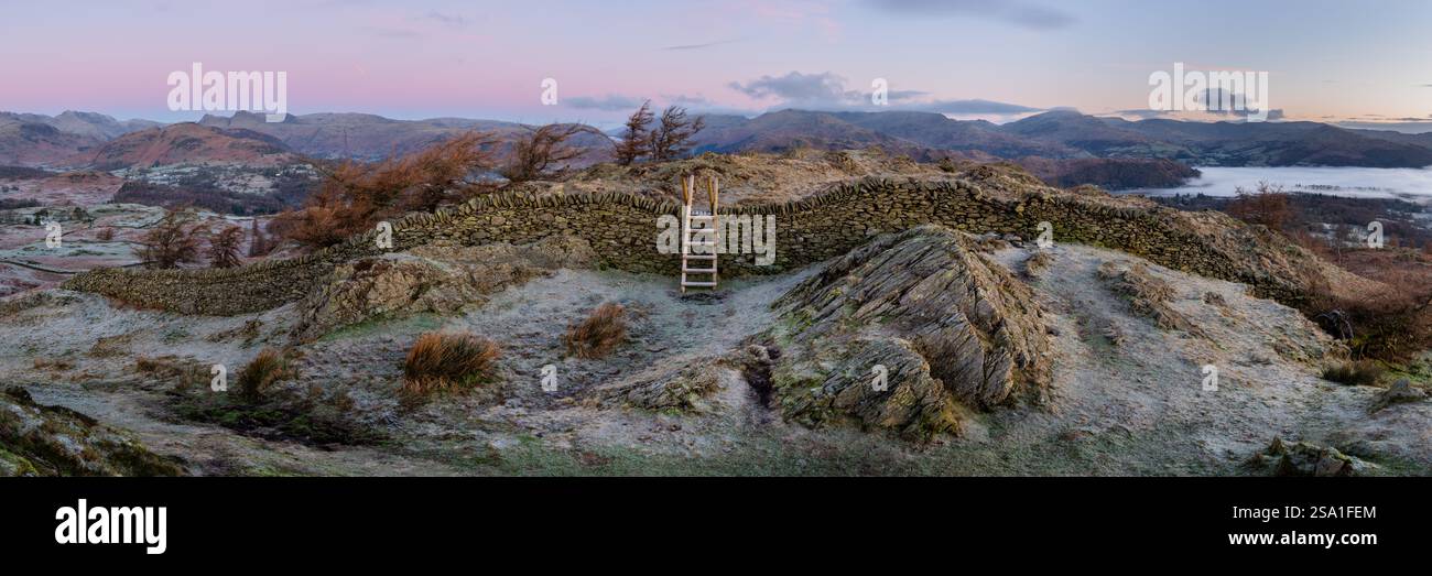 Panorama del Lake District all'alba visto dalla falesia nera con stile di legno sopra un muro di pietra. Vedute aeree verso Windermere e Langdale. Foto Stock