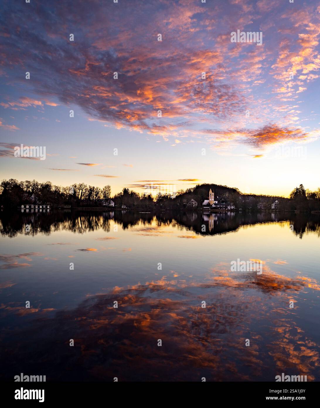 Un lago tranquillo al tramonto, che riflette nuvole e alberi colorati. Un piccolo edificio e' visibile sulla riva, circondato dalla natura. Il cielo è dipinto con Foto Stock