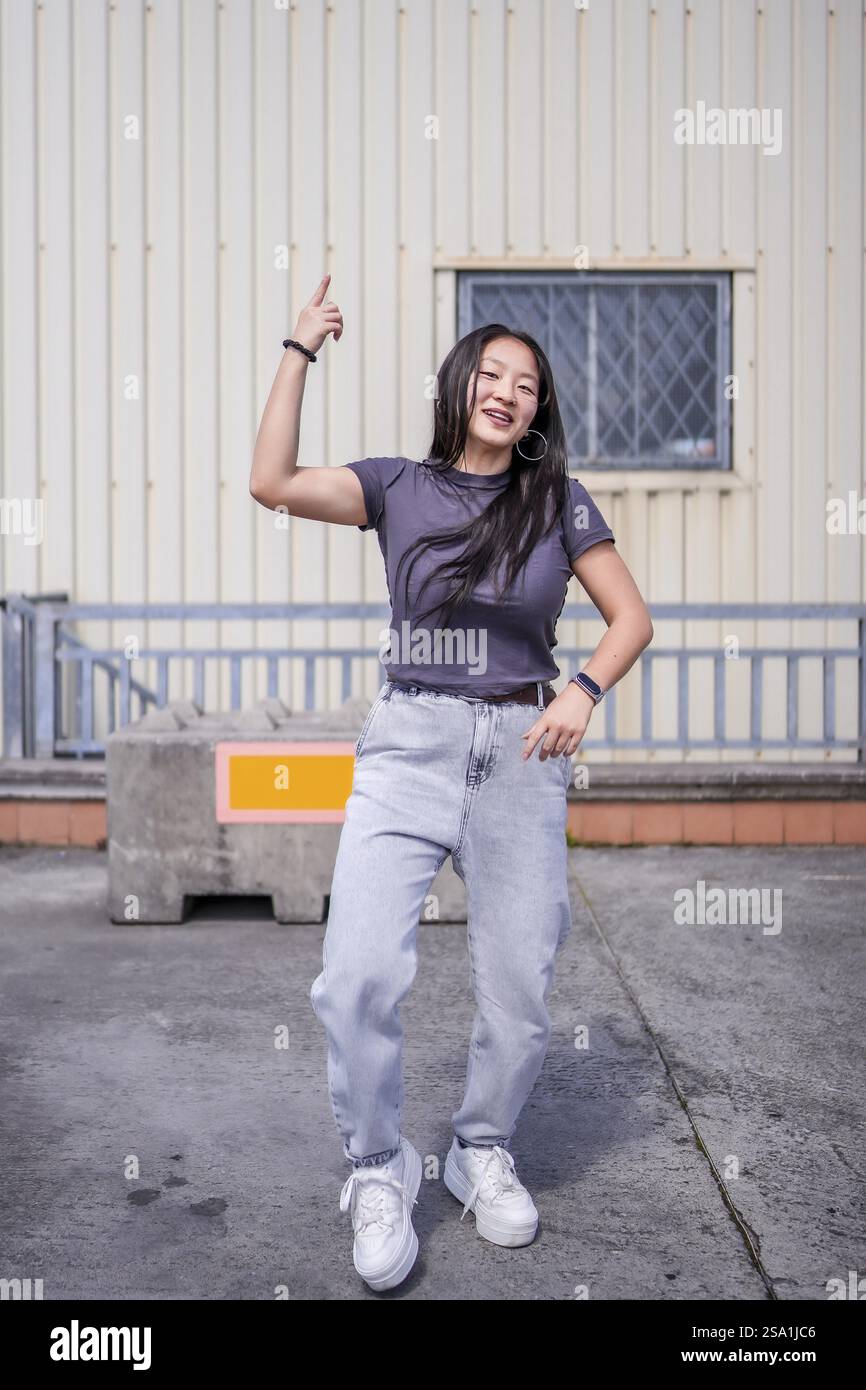 Foto verticale di una giovane donna asiatica che ballava musica urbana all'aperto accanto a un edificio industriale Foto Stock