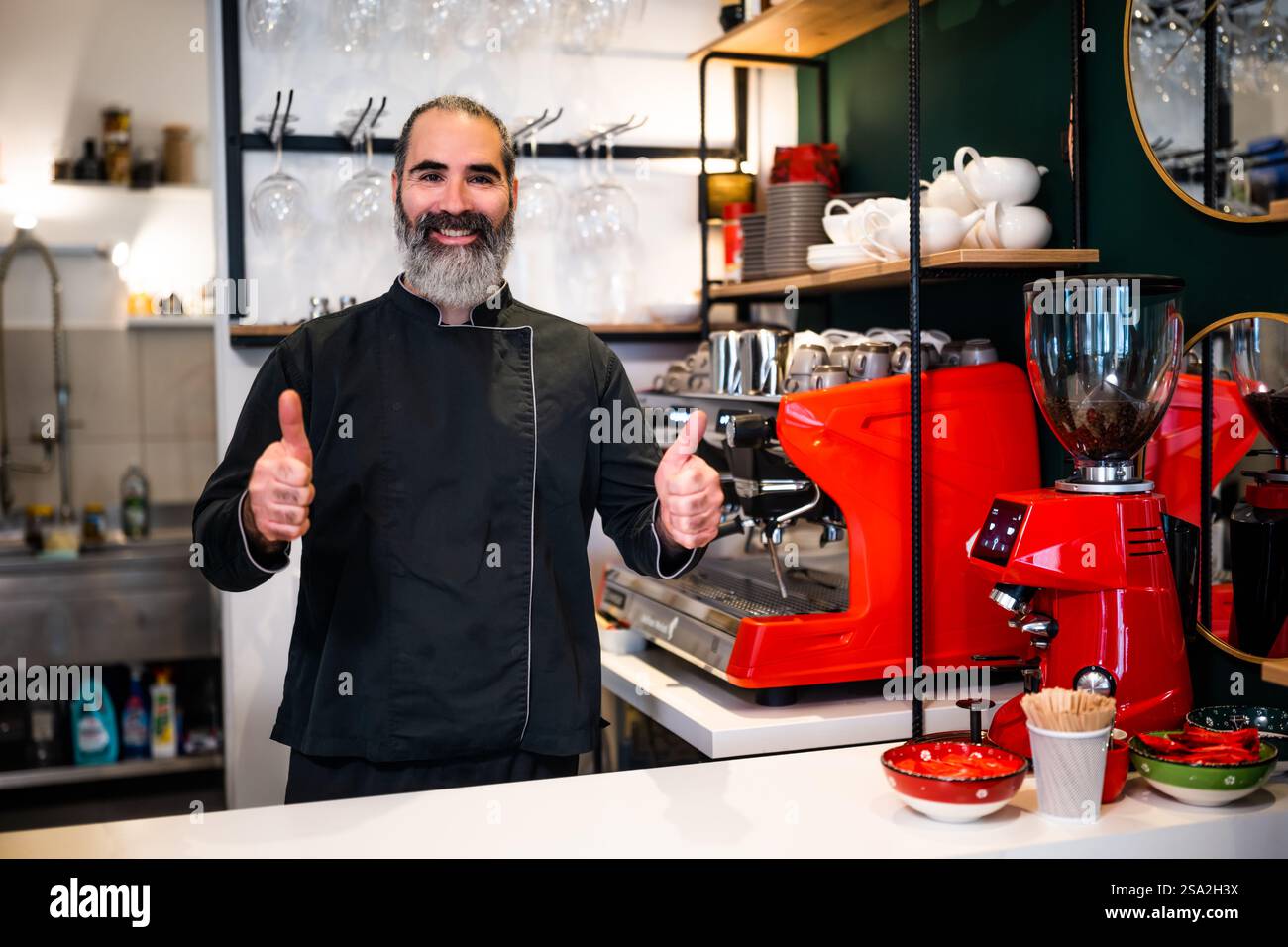 Barista professionista in grembiule nero che lavora al ristorante. Ritratto di barman felici che sta preparando il caffè nel suo bar. Foto Stock
