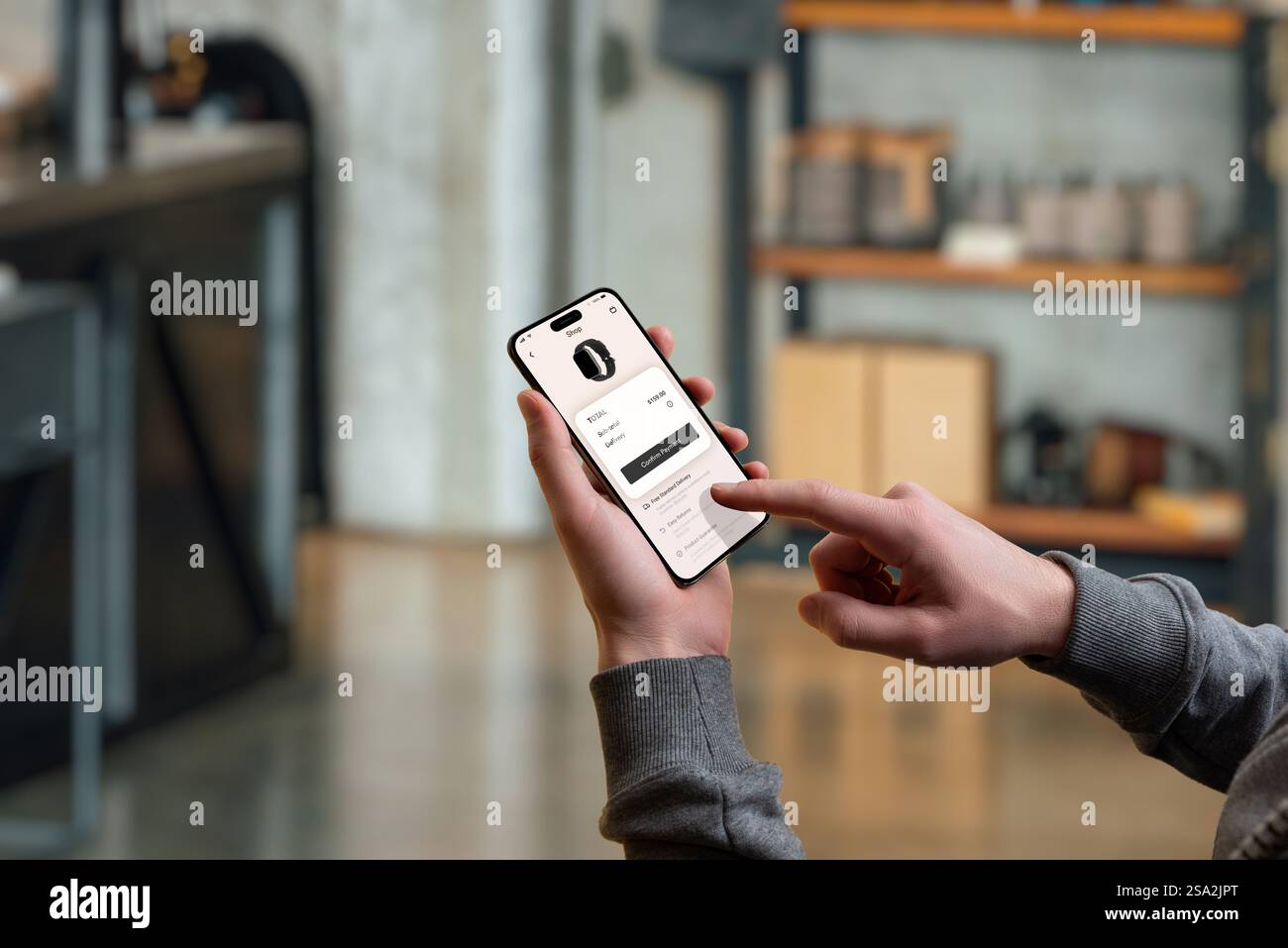 Mano a confermare l'acquisto di uno smartwatch su uno smartphone tramite una moderna app di e-commerce. L'ambiente è accogliente Foto Stock