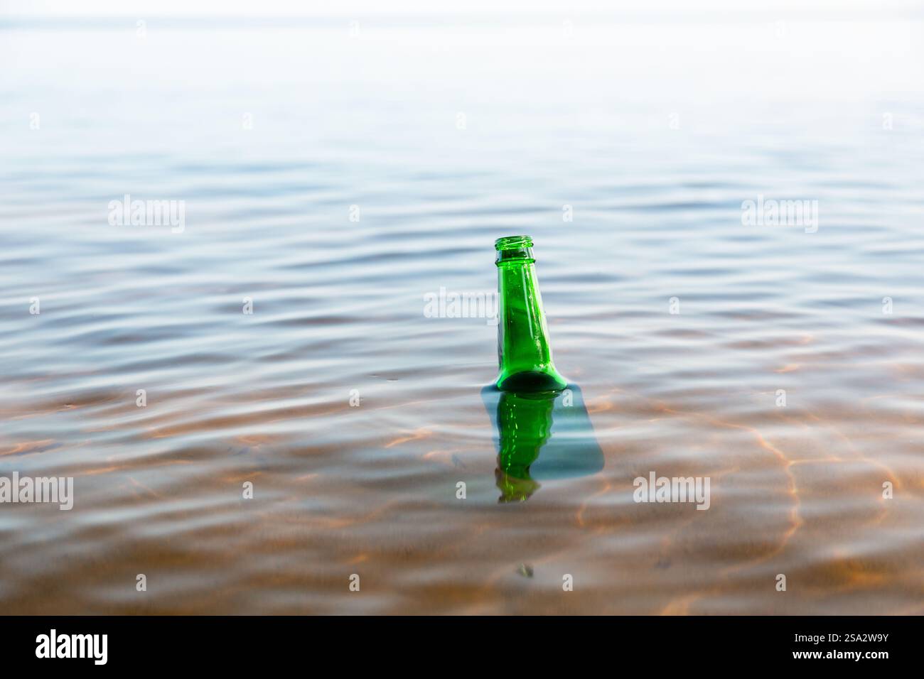 Bottiglia di vetro verde che galleggia in un fiume, collo di bottiglia visto sulla superficie dell'acqua. Concetto di protezione ambientale e controllo dei rifiuti. Foto Stock