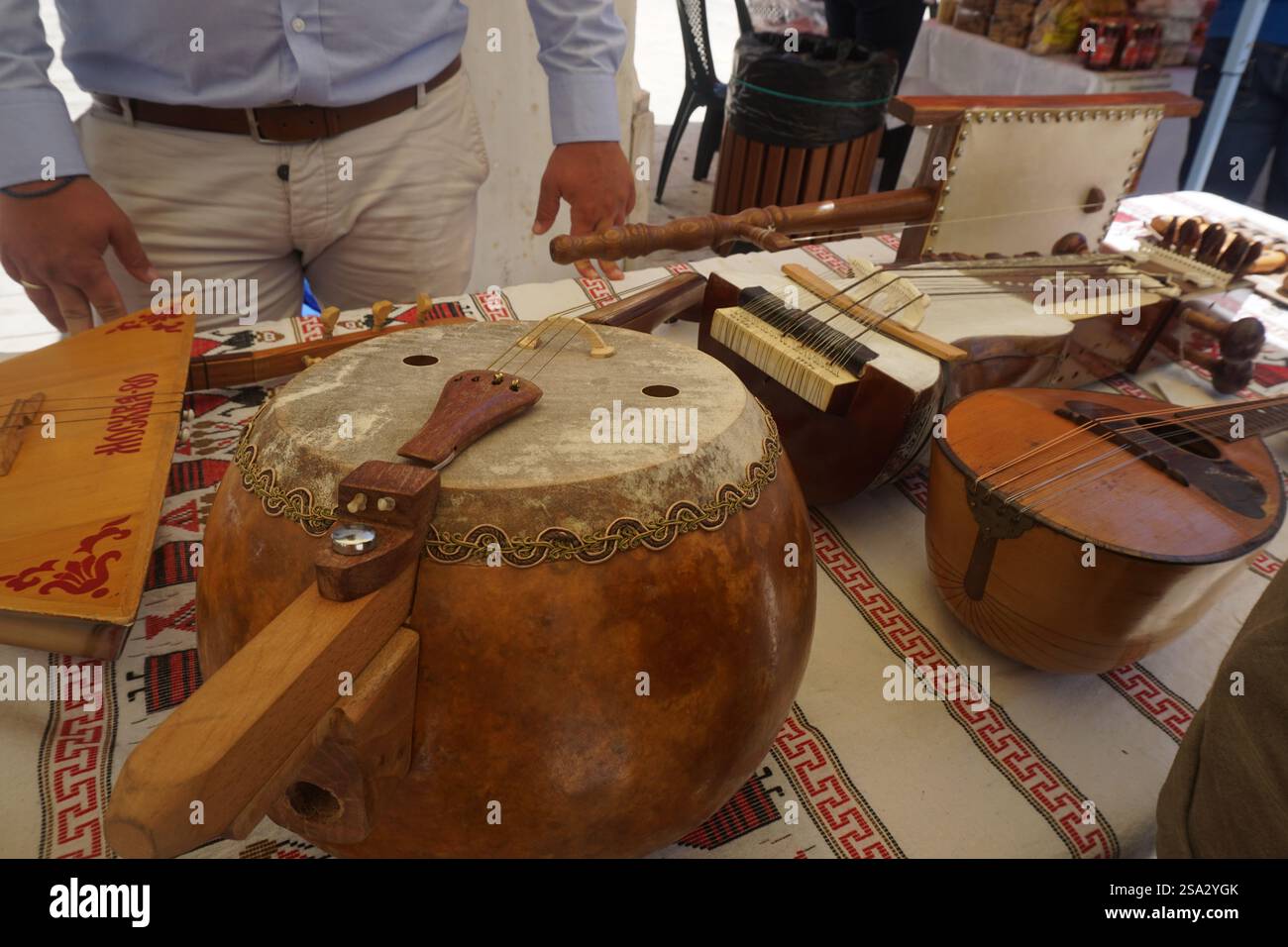 Strumenti musicali tradizionali, strumenti a fiato, archi, percussioni collocati su un tavolo in una mostra all'aperto e sullo sfondo un uomo in piedi Foto Stock