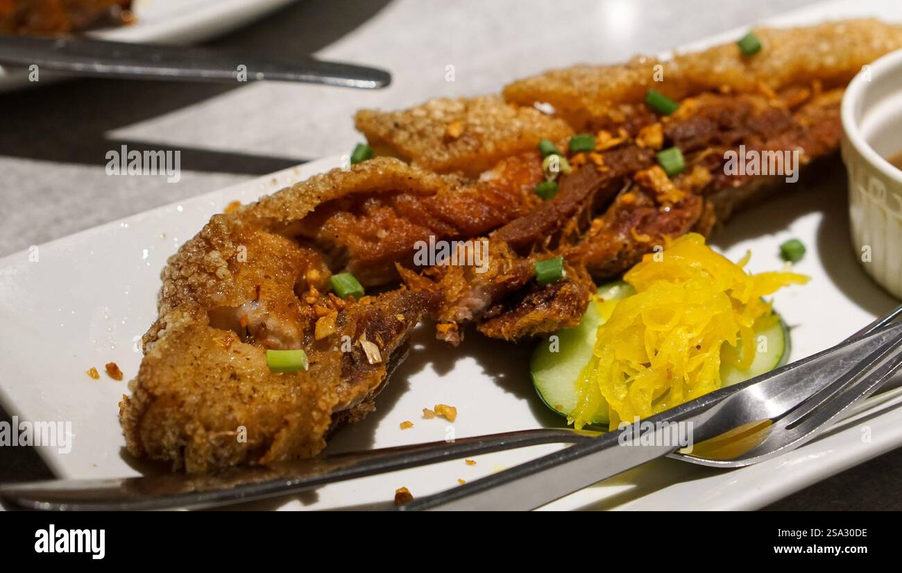 Un appetitoso piatto fritto di pancetta di maiale con pelle dorata croccante e carne tenera, servito in un ristorante a Iloilo, Filippine, che offre un'authe Foto Stock