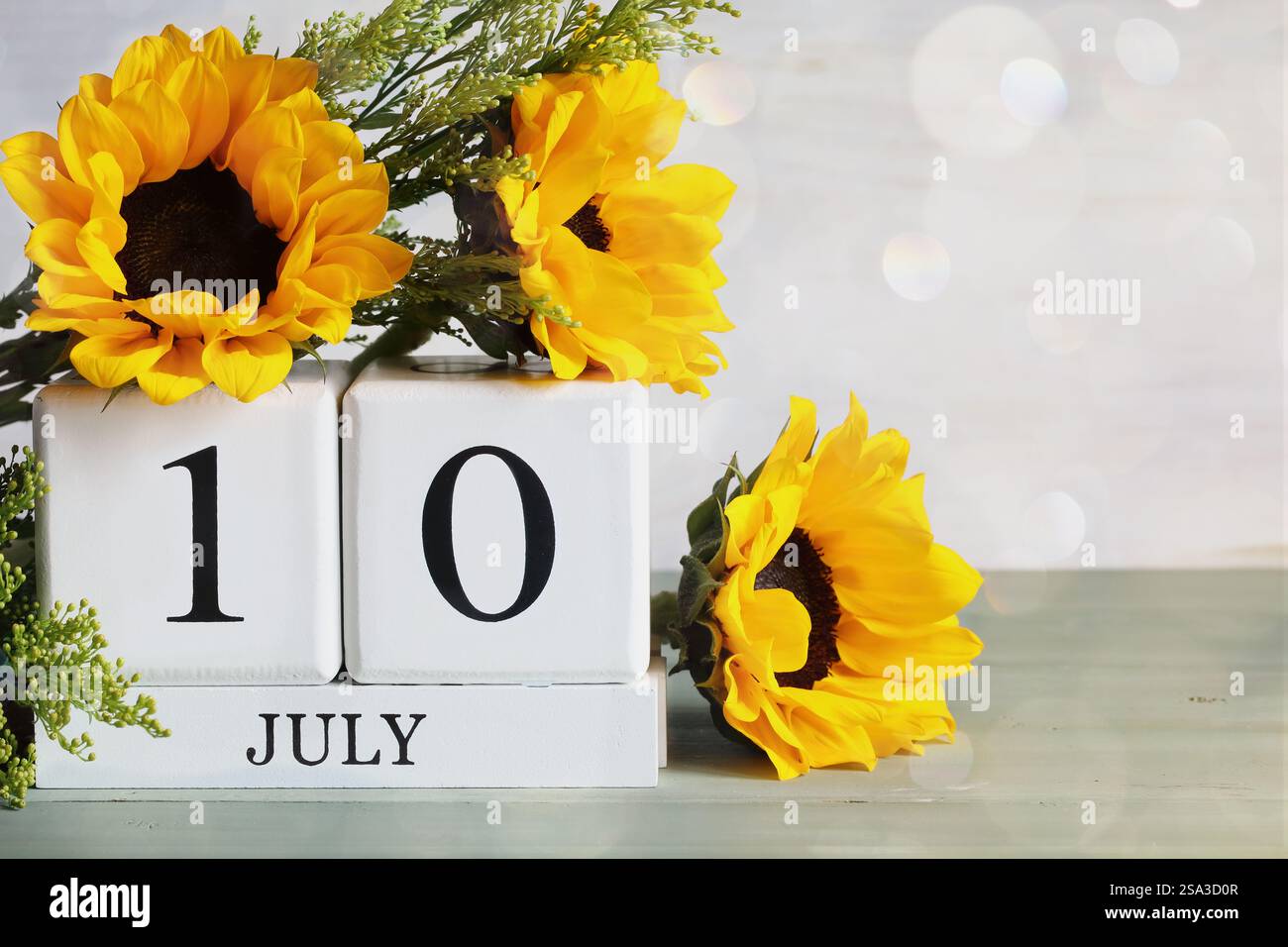 U. S. Energy Independence Day. Blocchi di calendario in legno bianco con la data del 10 luglio e bel bouquet di girasole con bokeh. Messa a fuoco selettiva. Foto Stock