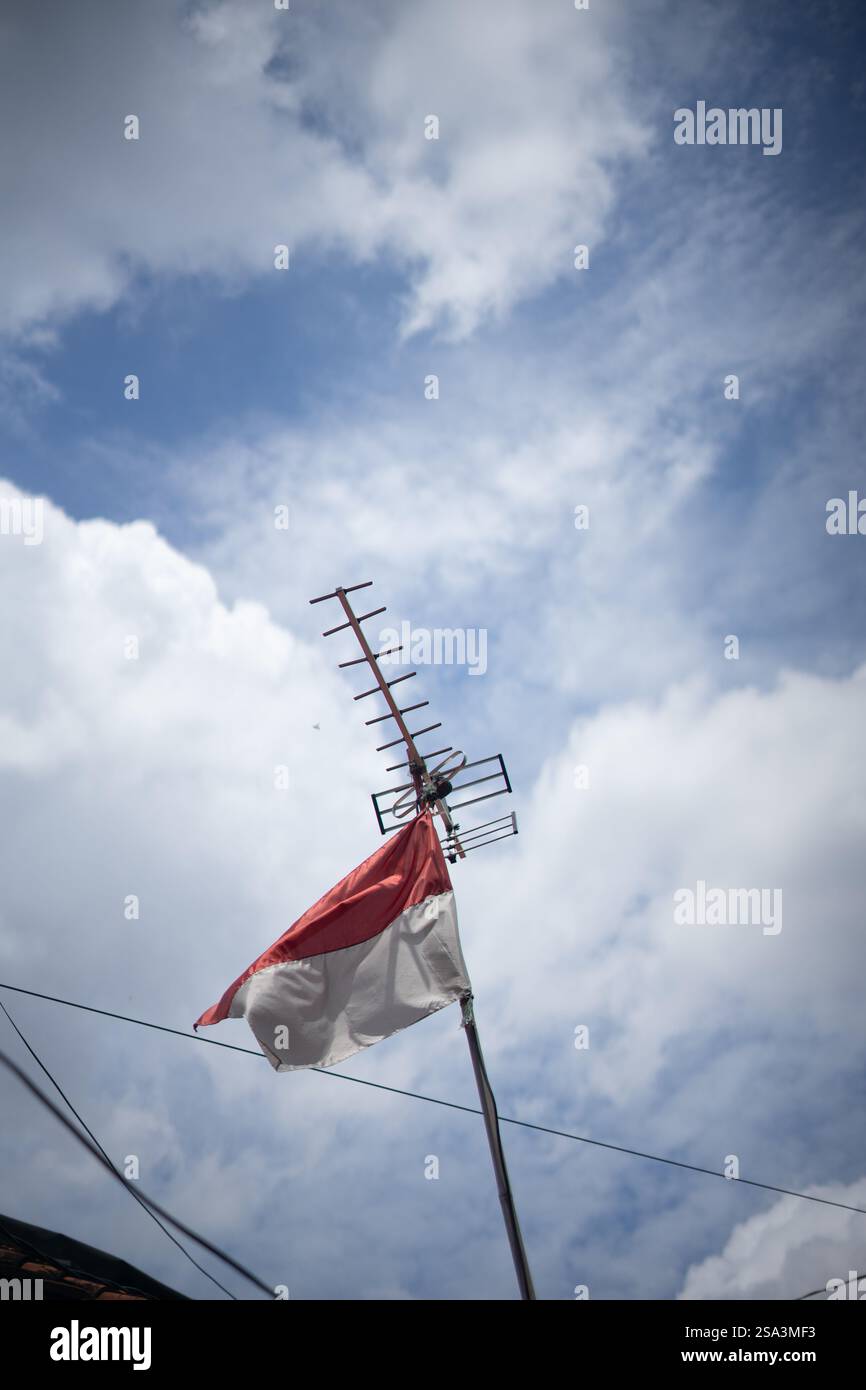 Bandiera indonesiana che sventola orgogliosamente sotto un'antenna televisiva contro un cielo nuvoloso. Foto Stock