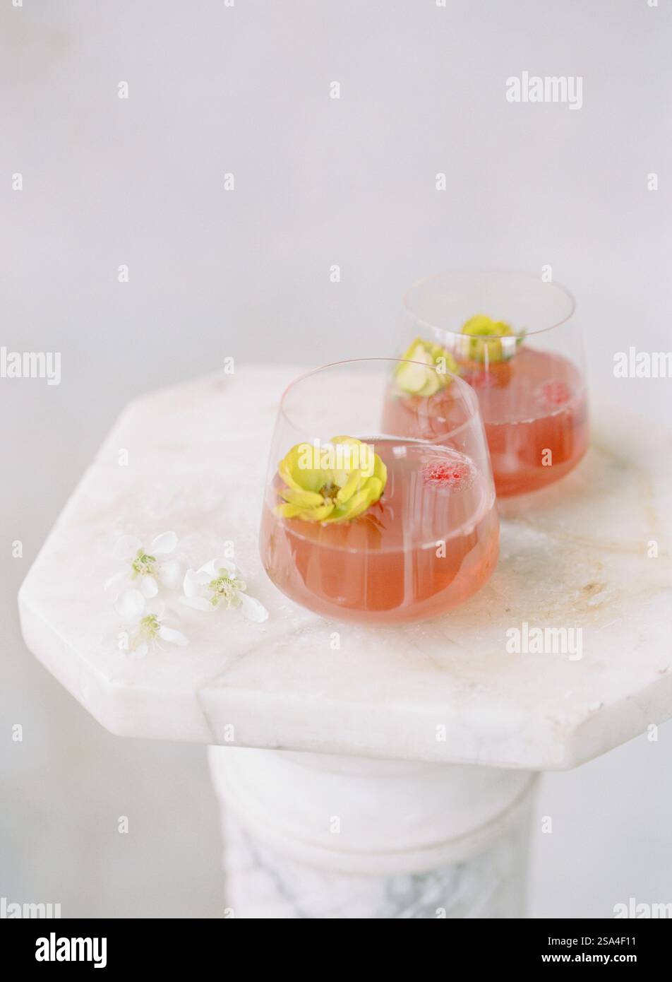 Due eleganti cocktail con decorazioni floreali poggiano su un piedistallo in marmo liscio. Le bevande sono caratterizzate da tonalità rinfrescanti, perfette per una festa estiva. Foto Stock