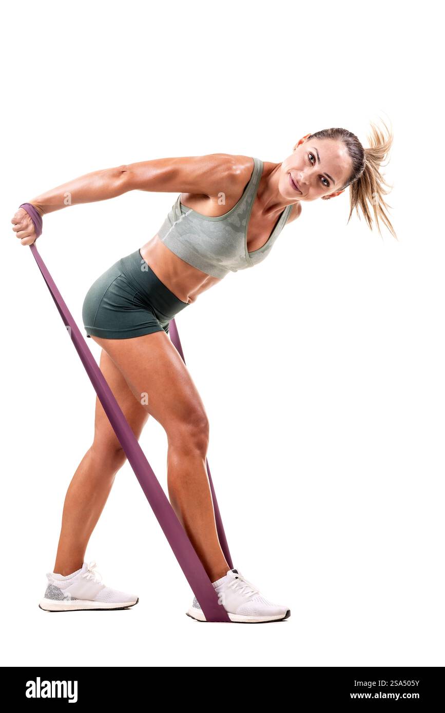 Donna atletica sicura di sé che dimostra l'esercizio della fascia di resistenza in uno studio luminoso, enfatizzando tono, forza e stile di vita sano. Foto Stock
