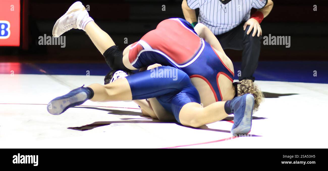 Due lottatori si impegnano in una partita competitiva su un tappeto di wrestling sotto le luci dell'arena. Foto Stock