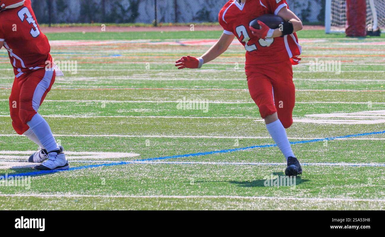 Un giovane giocatore di calcio con l'uniforme rossa corre abilmente con il calcio su un campo verde vivace durante una partita competitiva. Foto Stock