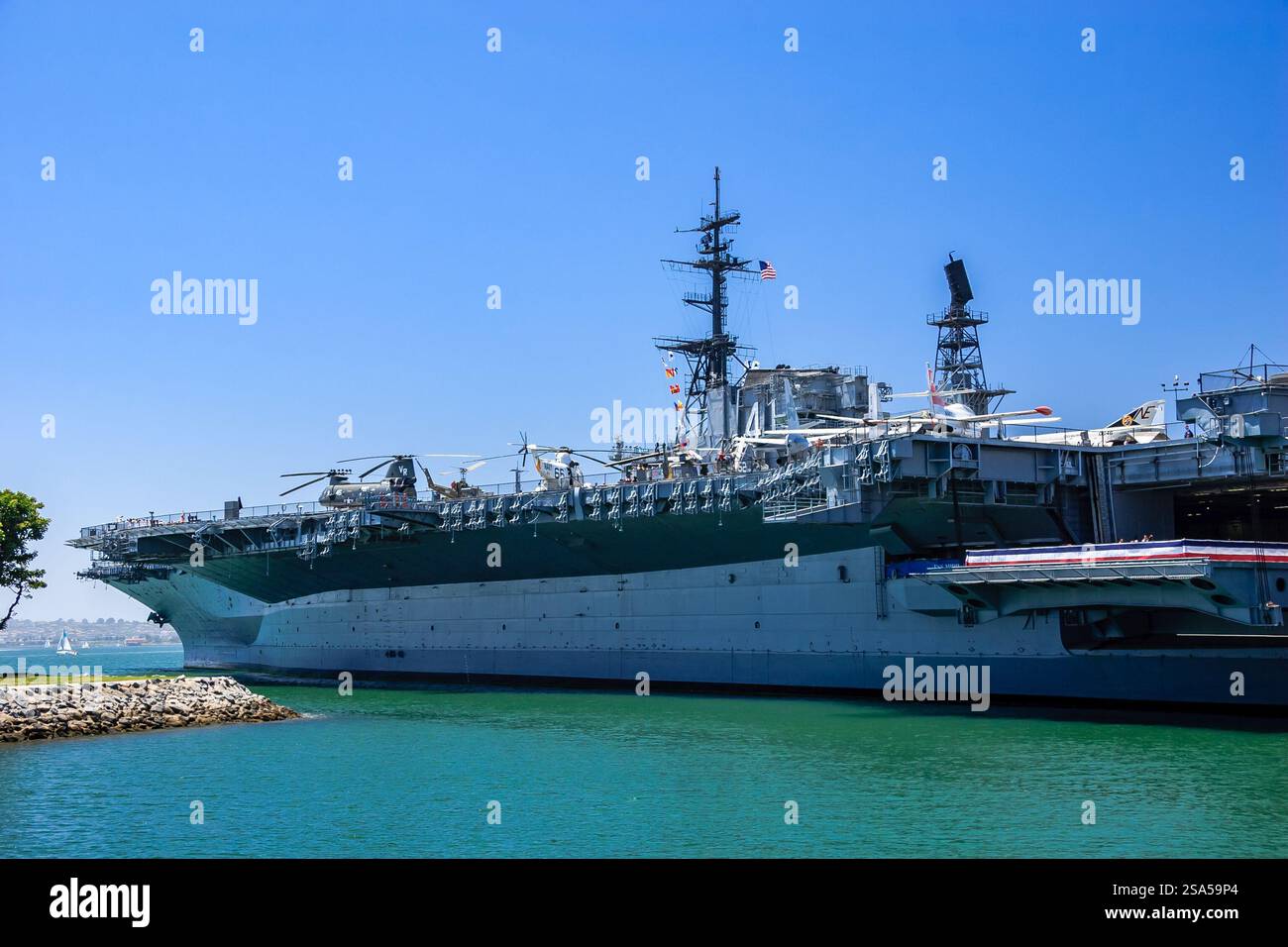 Una grande nave della marina è ancorata in un corpo d'acqua. La nave è circondata da un cielo blu e l'acqua è calma Foto Stock