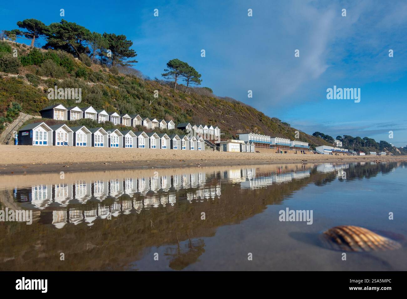 Le capanne costeggiano il litorale e si riflettono in acque poco profonde durante una giornata invernale luminosa a Branksome Chine Beach a Bournemouth, Dorset, Inghilterra, Regno Unito Foto Stock