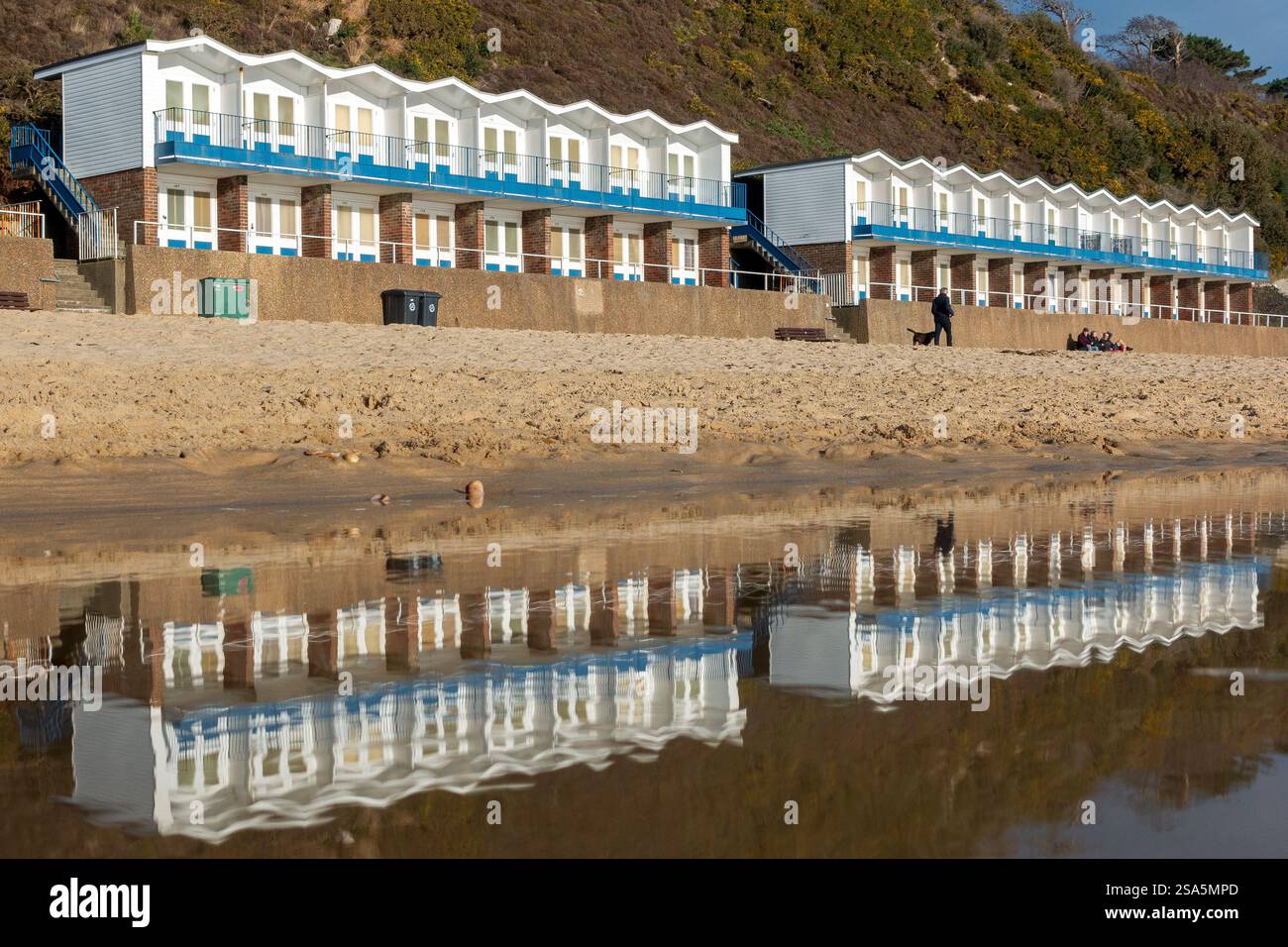 Le capanne costeggiano il litorale e si riflettono in acque poco profonde durante una giornata invernale luminosa a Branksome Chine Beach a Bournemouth, Dorset, Inghilterra, Regno Unito Foto Stock