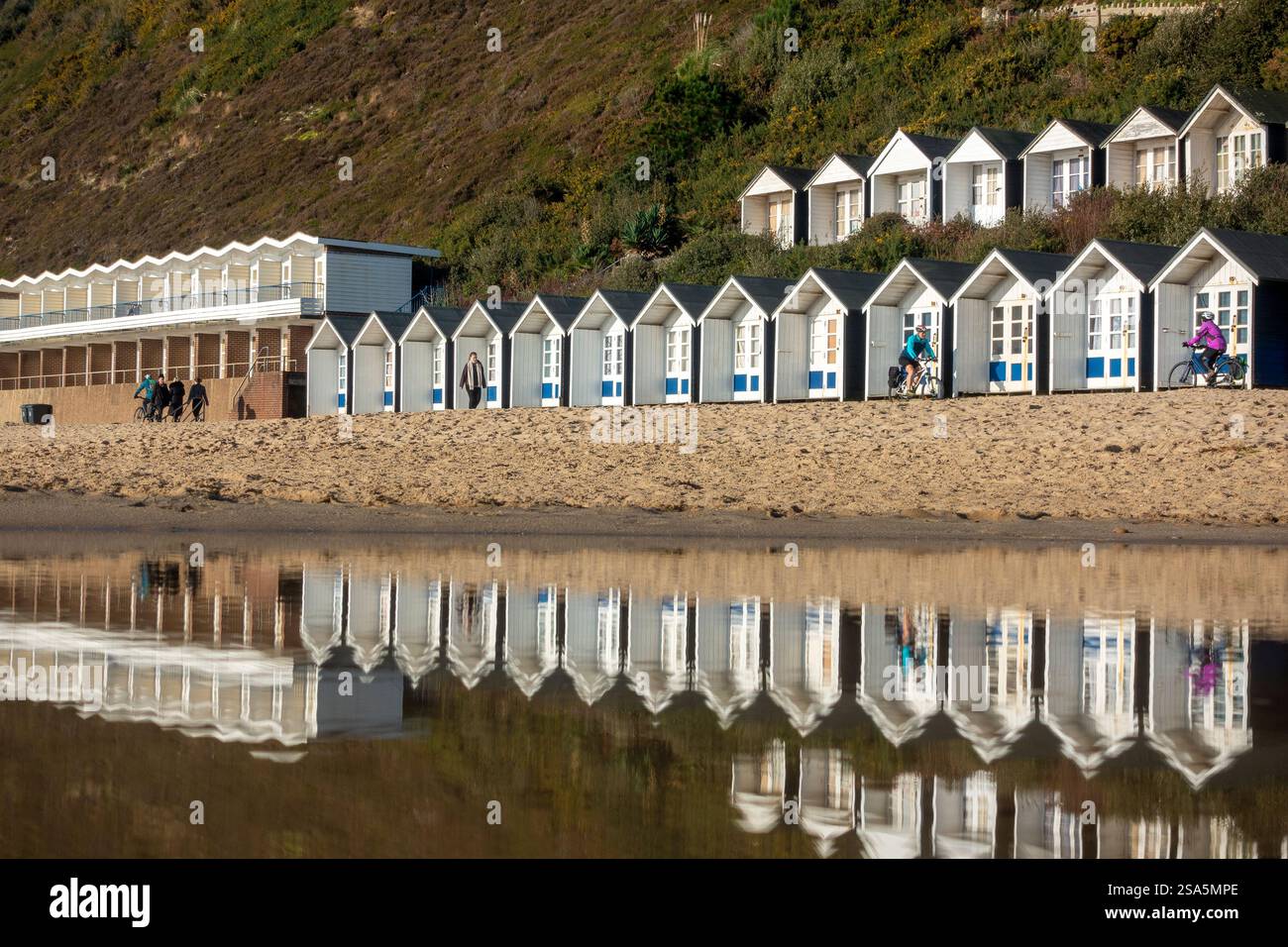 Le capanne costeggiano il litorale e si riflettono in acque poco profonde durante una giornata invernale luminosa a Branksome Chine Beach a Bournemouth, Dorset, Inghilterra, Regno Unito Foto Stock