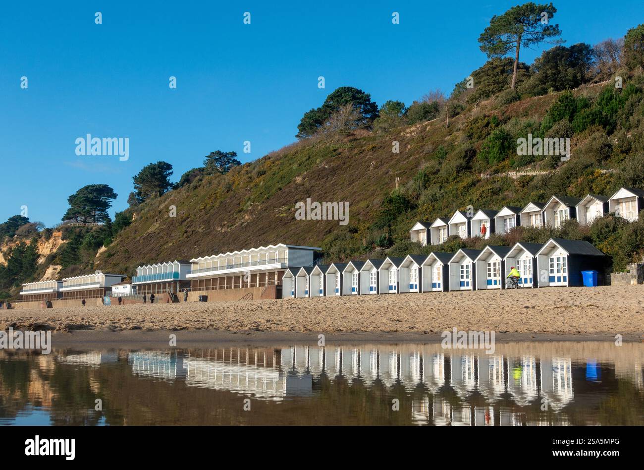 Le capanne costeggiano il litorale e si riflettono in acque poco profonde durante una giornata invernale luminosa a Branksome Chine Beach a Bournemouth, Dorset, Inghilterra, Regno Unito Foto Stock
