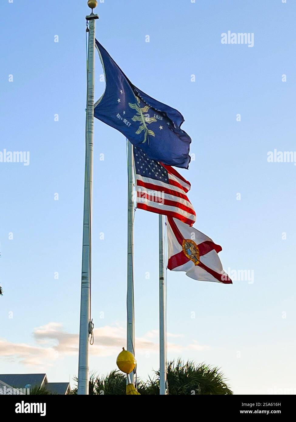 Le bandiere degli Stati Uniti, della Florida e di Key West volano contro un cielo notturno azzurro a Mallory Square, vicino all'attracco del terminal delle navi da crociera, a Key West, Florida. Foto Stock