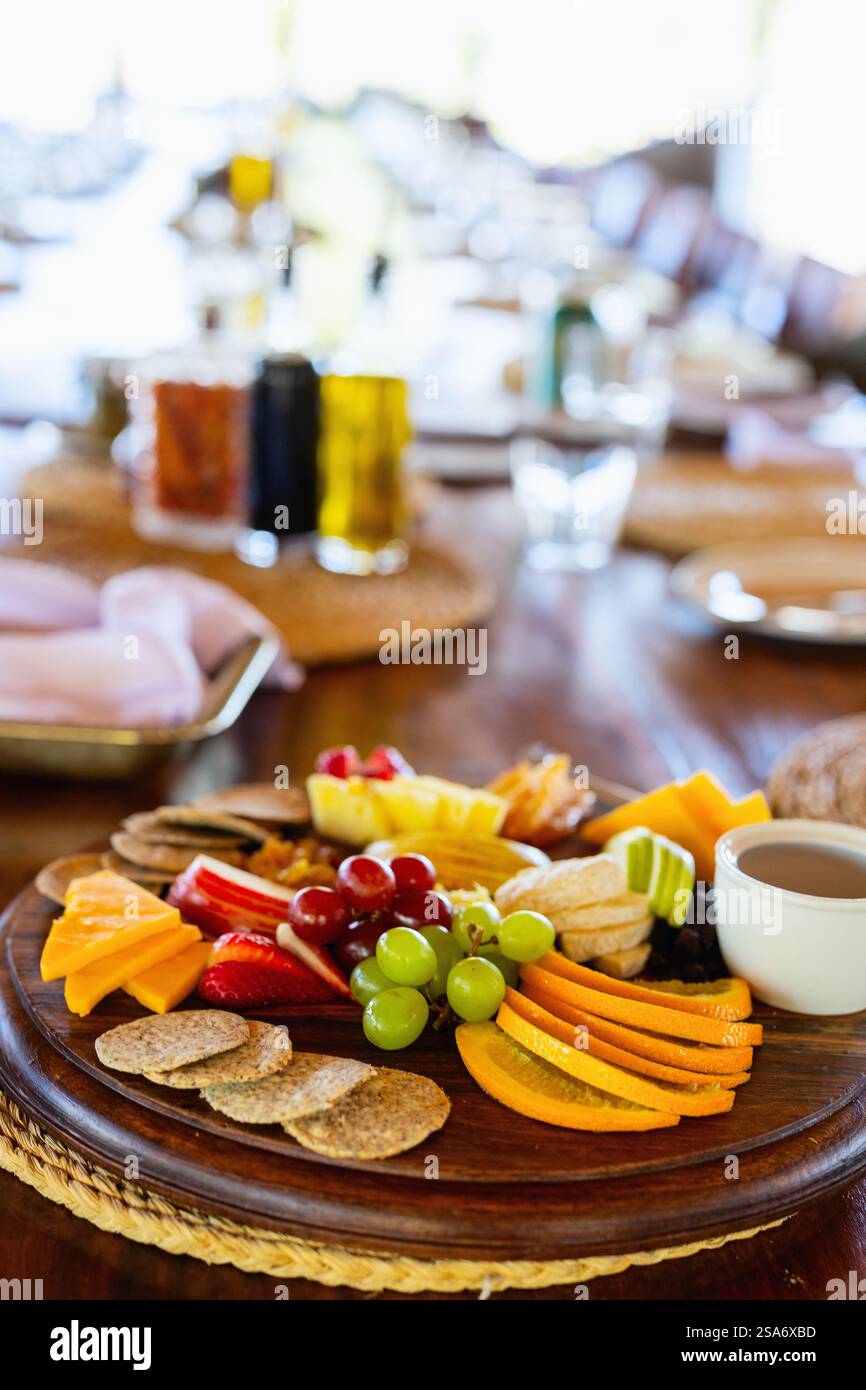 Un piatto ben organizzato con frutta fresca, formaggio, cracker e salse su un tavolo di legno per cenare, evocando un'atmosfera calda e invitante. Foto Stock