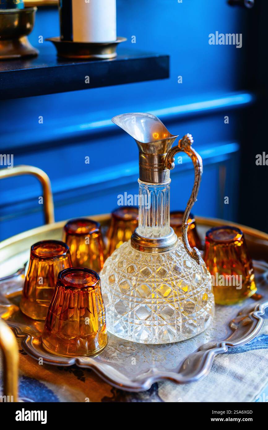 Decanter in cristallo decorato con manico decorativo e bicchieri da bibita color ambra disposti su un vassoio da portata in argento antico Foto Stock