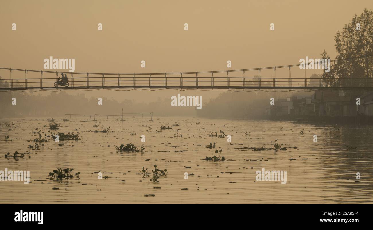 Gita in barca mattutina sul fiume Martapura al mercato galleggiante di Lok Baintan con ponte in legno e case sul lungofiume a Banjarmasin Foto Stock
