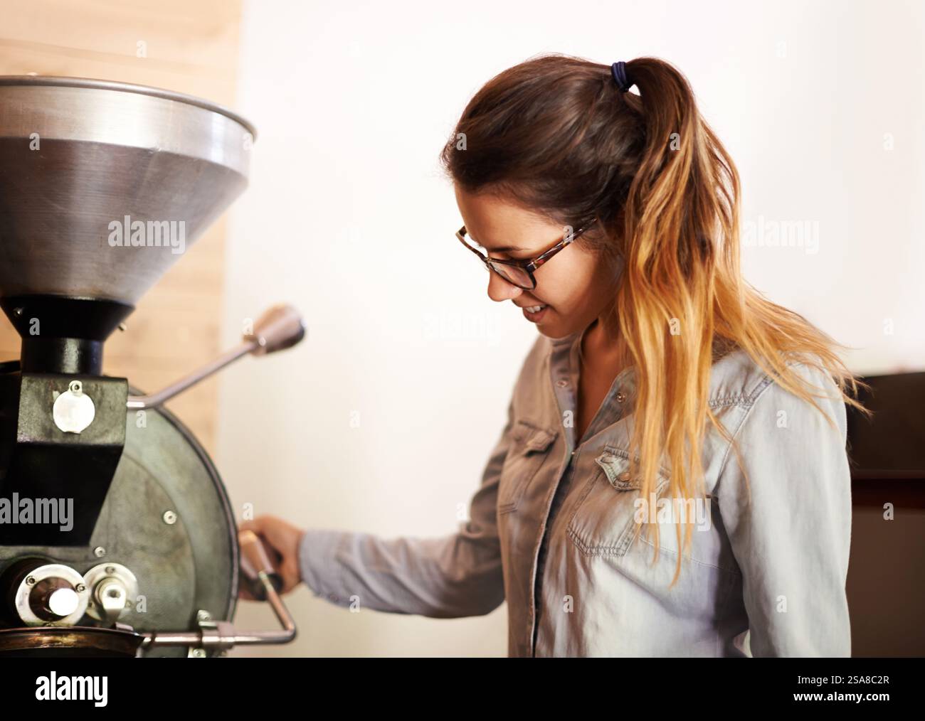 Macchina per caffè, donna e tostatura per la produzione, il controllo qualità e il processo di produzione nelle piccole imprese. Fabbrica, attrezzature e barista con Foto Stock