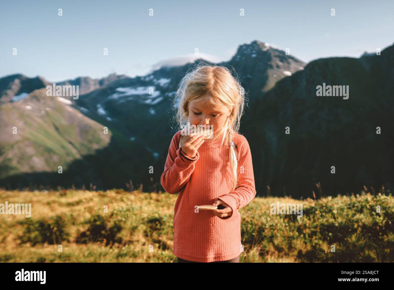 Bambino ragazza che mangia biscotti spuntini in montagna avventura viaggi in famiglia vacanze all'aperto stile di vita sano attivo 4 anni bambino biondo capelli esplorare Foto Stock