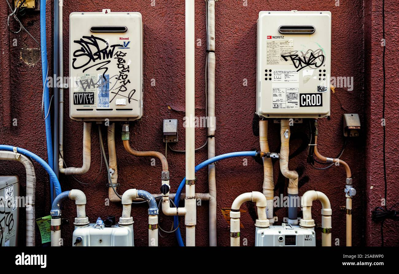 Vista ravvicinata di due scaldacqua sul lato di un edificio nella zona ovest di Tokyo, con vari adesivi e graffiti visibili sopra e intorno ad essi Foto Stock