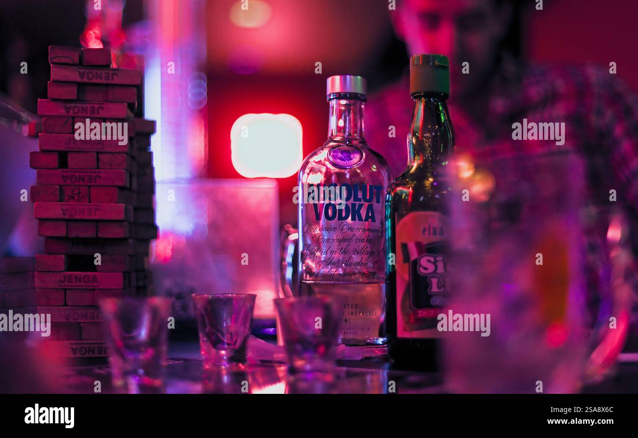 Parte di un bar in Giappone, illuminato da una luce rosa brillante, con bottiglie, bicchieri e un set Jenga visibile e un uomo sullo sfondo Foto Stock