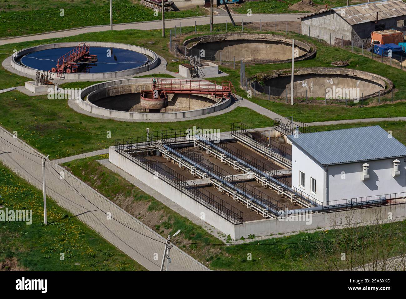 Un impianto di trattamento delle acque che espone diverse cisterne circolari e un edificio per le attrezzature, circondato da erba e sentieri, che illustra le infrastrutture Foto Stock