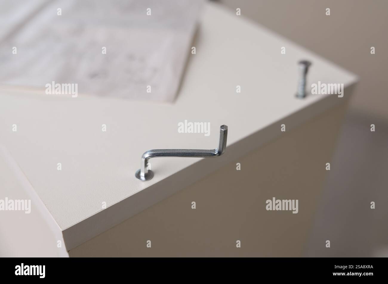 Assemblaggio di mobili. Primo piano di una chiave esagonale per serrare una vite su mobili di colore chiaro. Assemblaggio di mobili Foto Stock