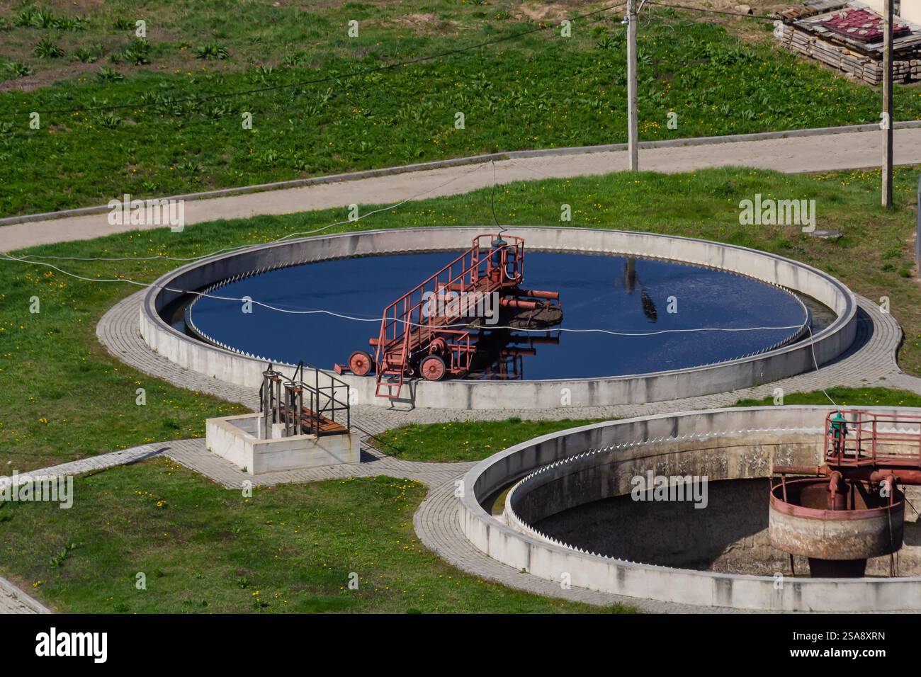 Un impianto di trattamento delle acque reflue è dotato di grandi serbatoi circolari riempiti di liquido scuro. Una piattaforma rossa è posizionata al centro di un serbatoio, con gr Foto Stock