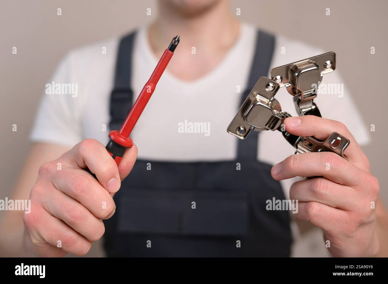 L'assemblatore di mobili tiene in mano una cerniera per mobili e un cacciavite, primo piano. Concetto di costruzione, tuttofare Foto Stock