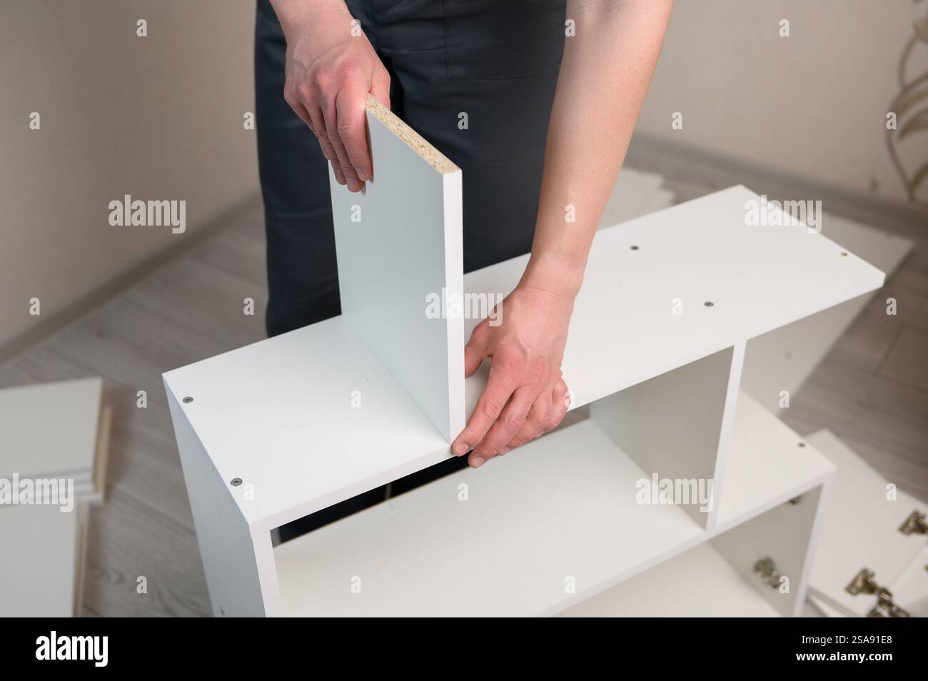 Assemblaggio di mobili. L'assemblatore di mobili prende un ripiano bianco, stringe la vite con una chiave esagonale. Collezionista di mobili. Concetto mobile, mobili Foto Stock