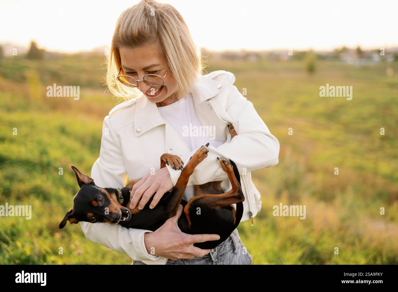 Una donna con gli occhiali tiene un terrier giocattolo russo dai capelli lisci tra le braccia mentre cammina, accarezzandolo. Concetto di amicizia tra uomo e cane, amore f Foto Stock