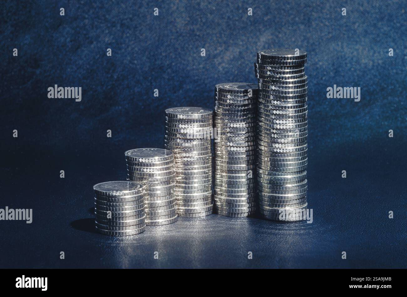 Monete d'argento lucide in pile su sfondo blu. Idea di crescita. Finanza, affari, risparmi, tasso di deposito Foto Stock