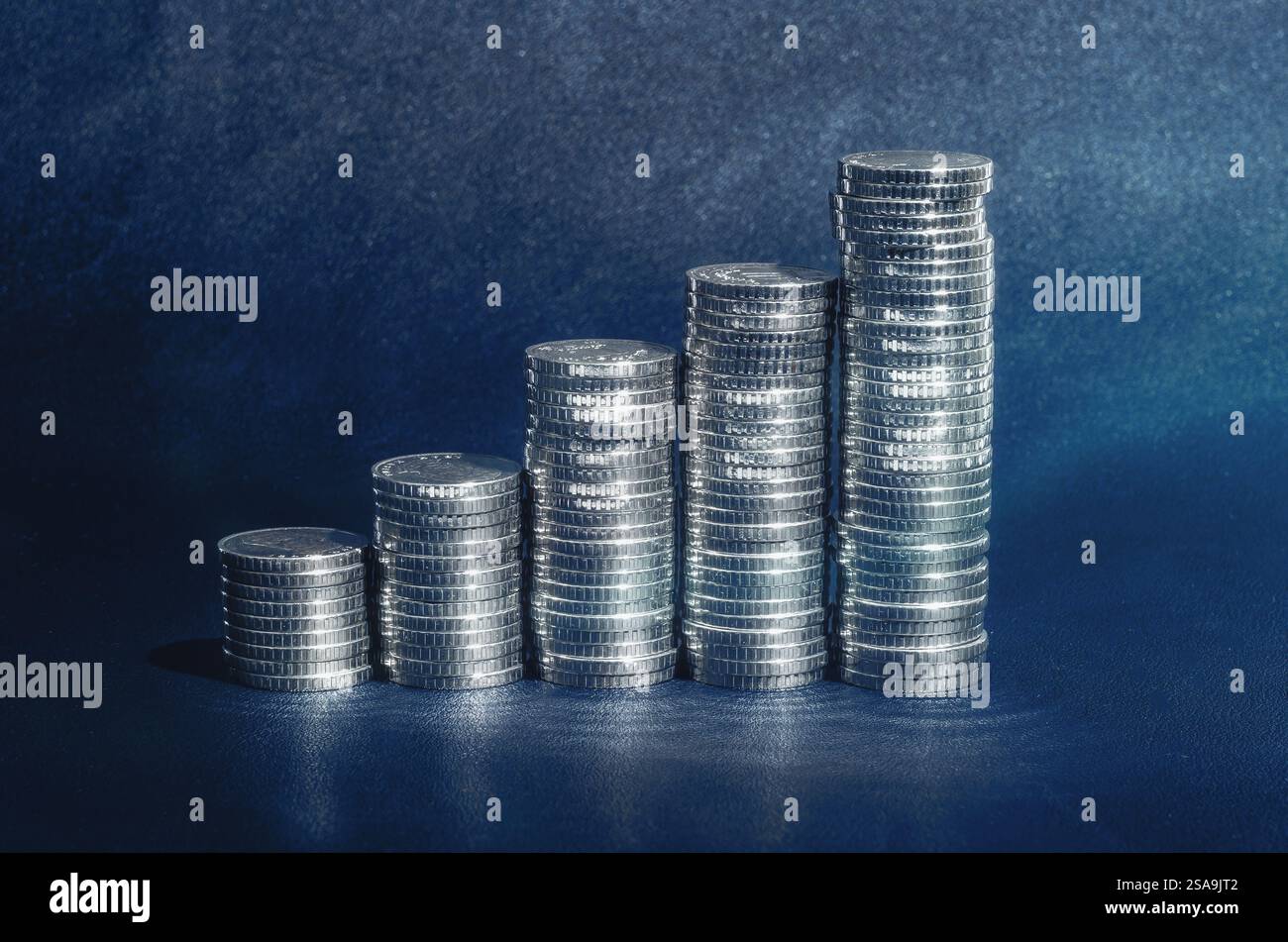 Monete d'argento lucido in pile su sfondo blu scuro. Concetto di crescita. Finanza, affari, risparmi, tasso di deposito Foto Stock