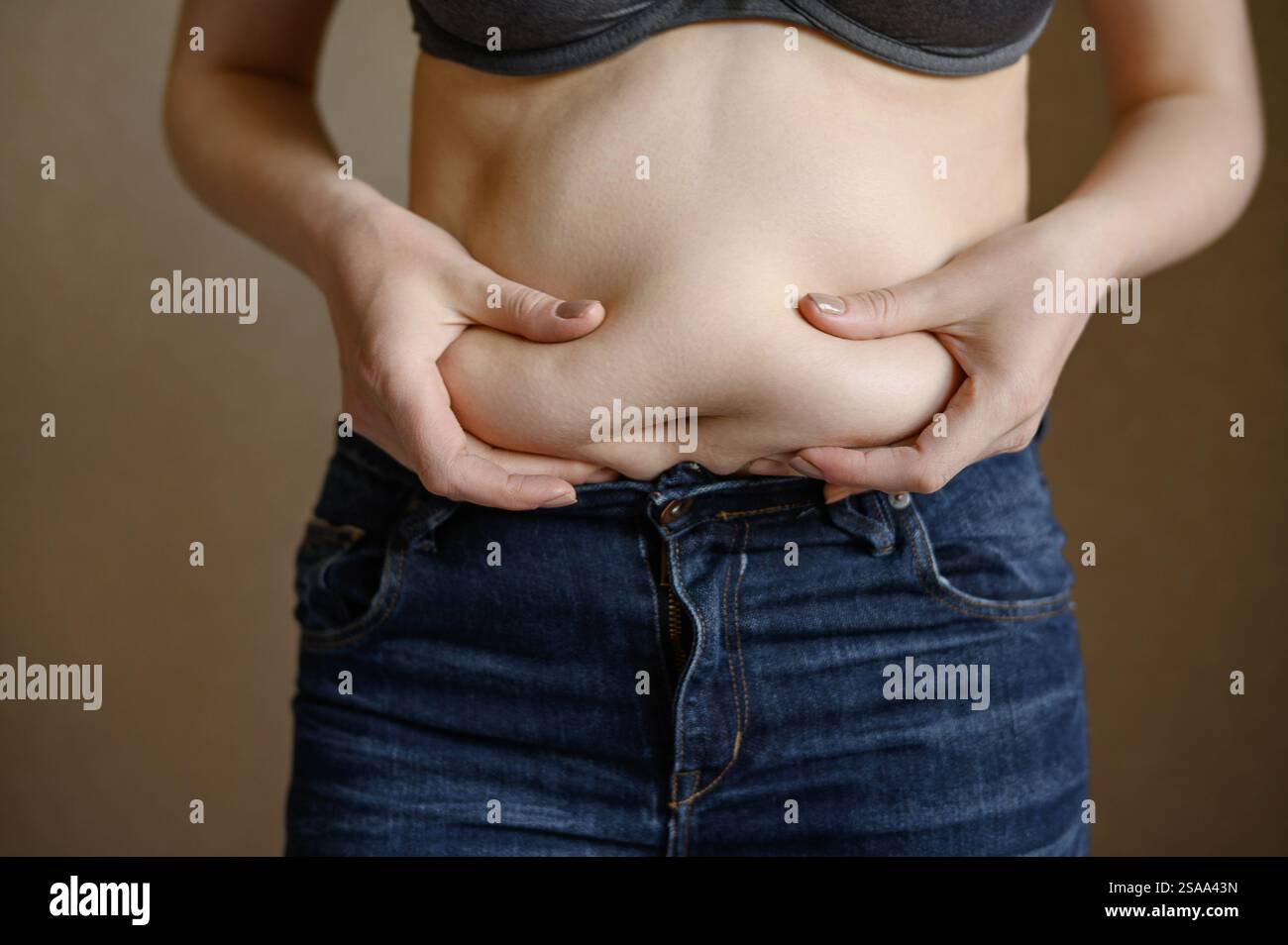 Una donna grassa in jeans con una pancia sporgente tocca il grasso che si piega sullo stomaco, primo piano. Stile di vita, concetto di dieta, perdita di peso, obesità, mancanza di exe Foto Stock