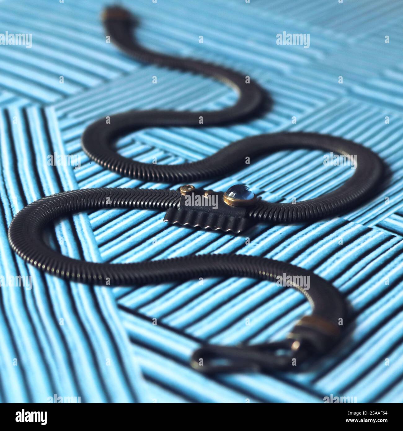 La collana in argento nero si avvolge su una superficie blu testurizzata, somigliante a un serpente. Foto Stock