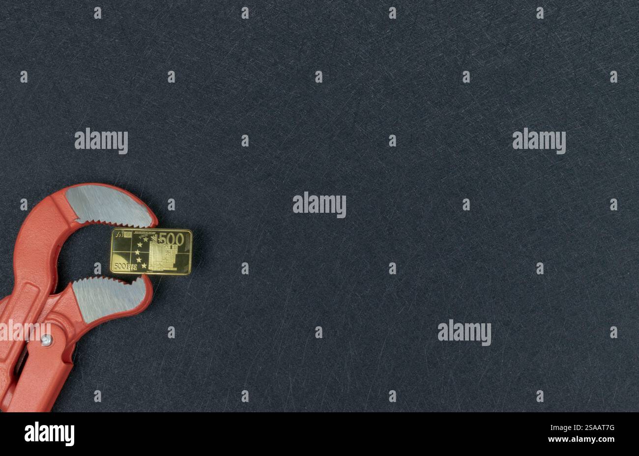 Moneta da 500 Euro dorata nelle ganasce di una chiave per tubi. Valute che perdono valore. Svalutazione della placca in metallo dorato in Europa. Foto Stock