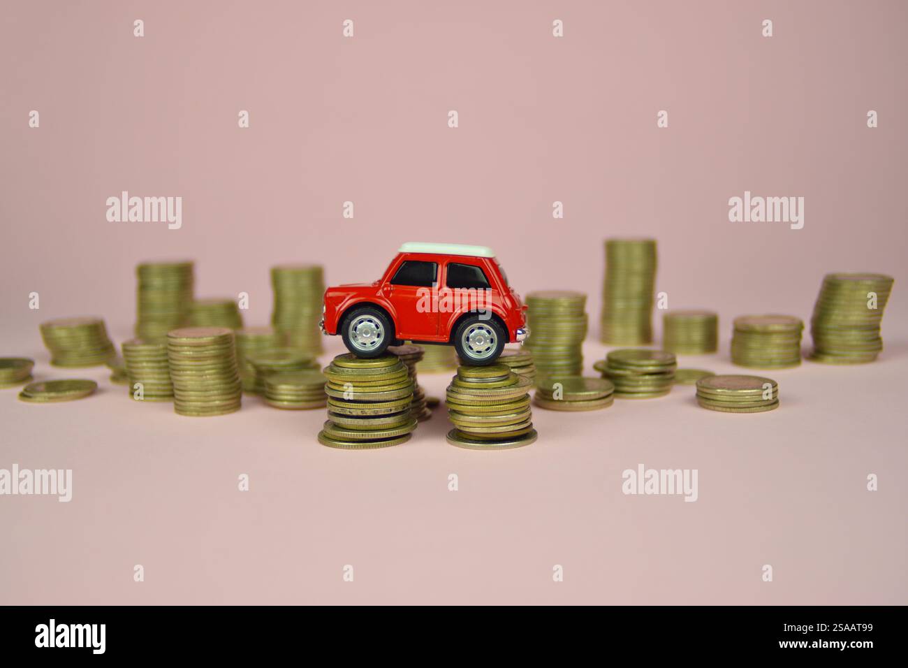 Giocattolo rosso per auto su pile di monete. Sfondo rosa. I costi dell'auto si accumulano. Prezzo, manutenzione, riparazione, assicurazione, credito Foto Stock