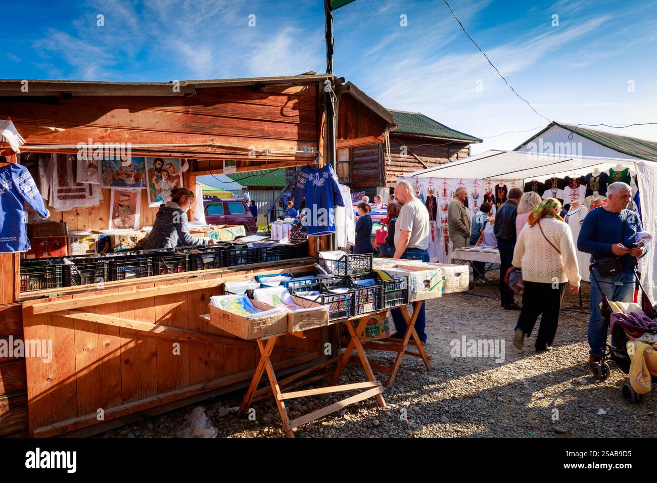 Un gruppo di persone è riunito intorno a un banco di legno con vari oggetti in vendita. L'atmosfera e' vivace e vivace, con gente che naviga e fa shopping Foto Stock